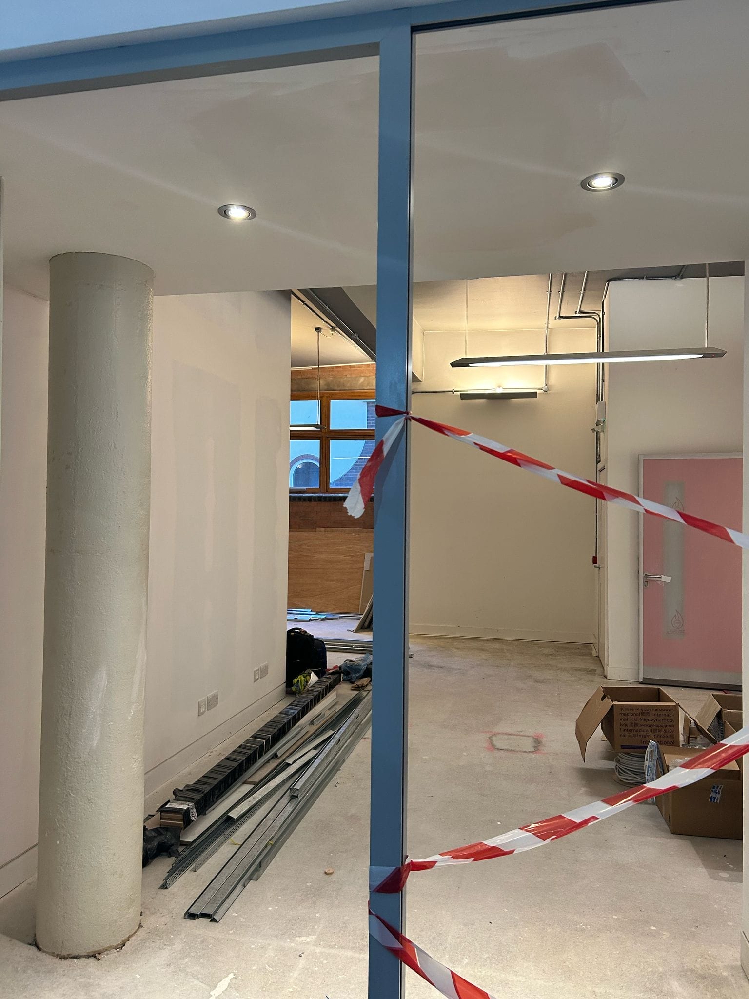 Graeae's old office space is under construction. Red and white hazard tape is tied between metal poles. There are large strips of metal on the ground.